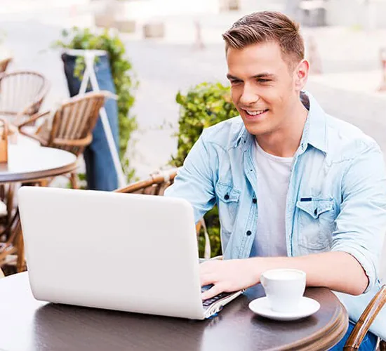 foto de un hombre sonriente que está sentado mirando hacía su laptop